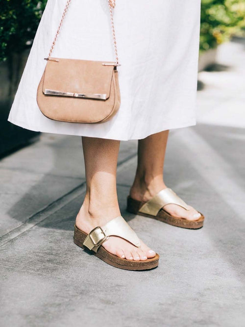 Foto de estilo de vida de una modelo usando las sandalias Itaca en color dorado, destacando un look brillante, relajado y con mucho estilo para el día a día.